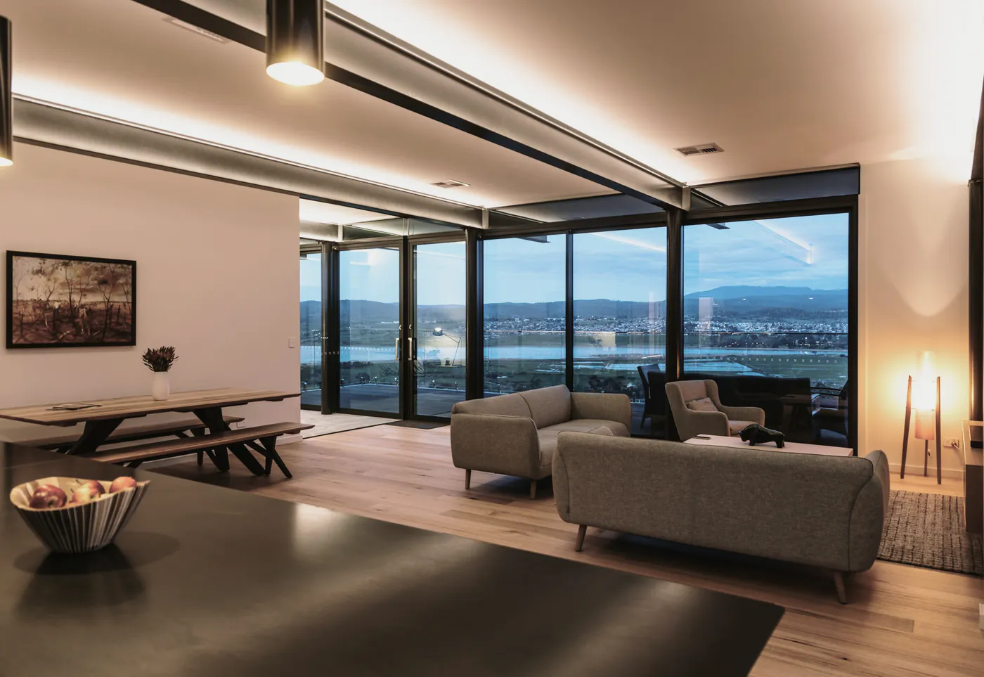 An open living and dining room with full height windows looking west over the bay