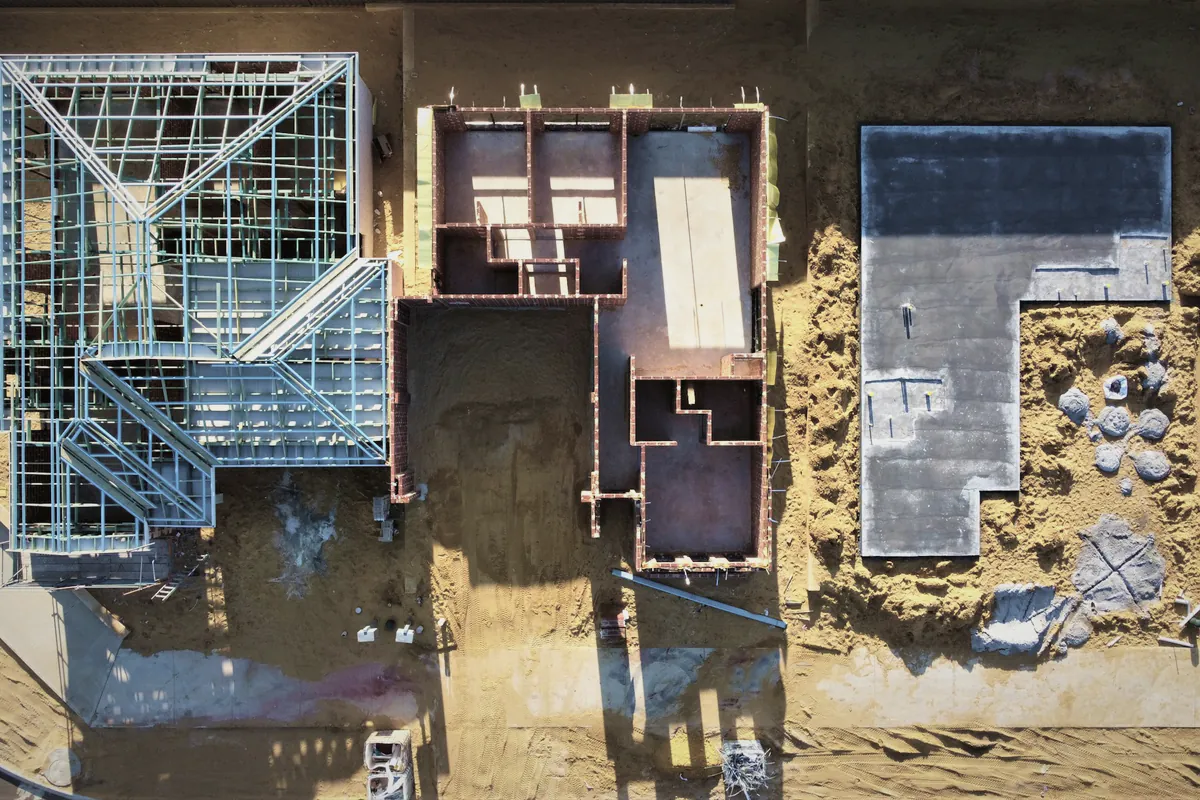 A building site from above: a steel roof frame, brick walls going up and a new slab next door