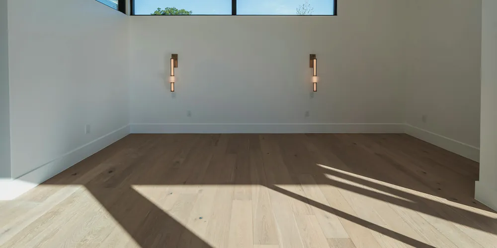 An empty room with oak floors and wall lights in the afternoon sun