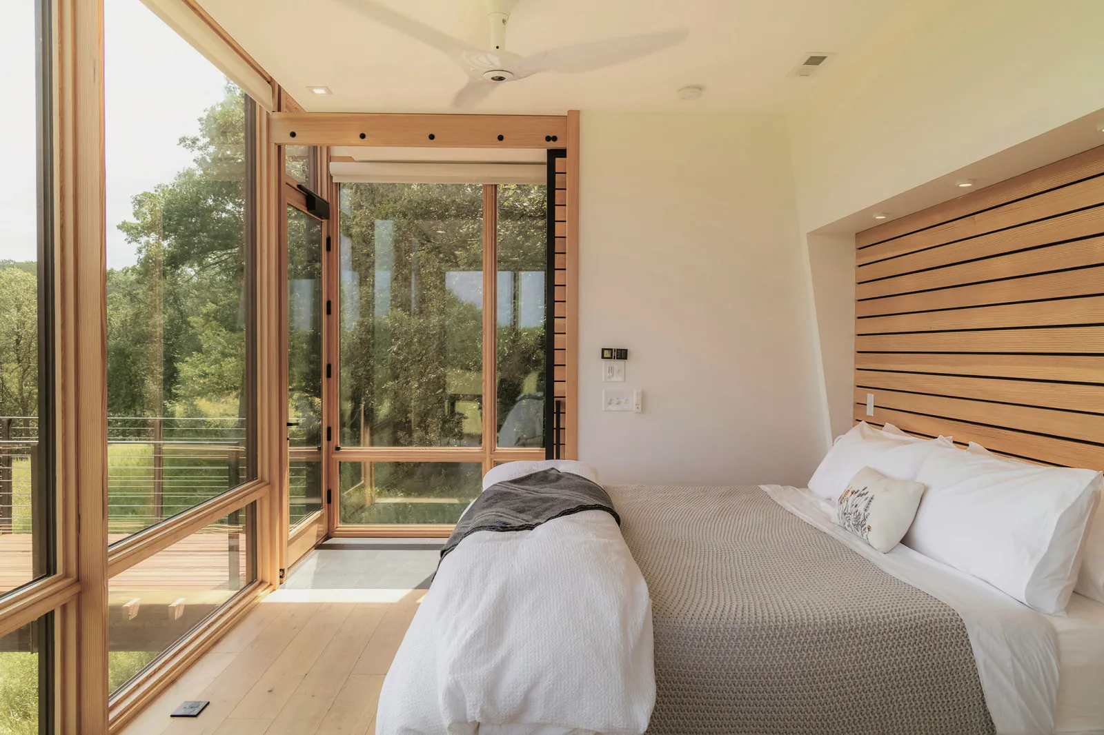 A bedroom with timber framed glass walls and a slatted cedar bedhead