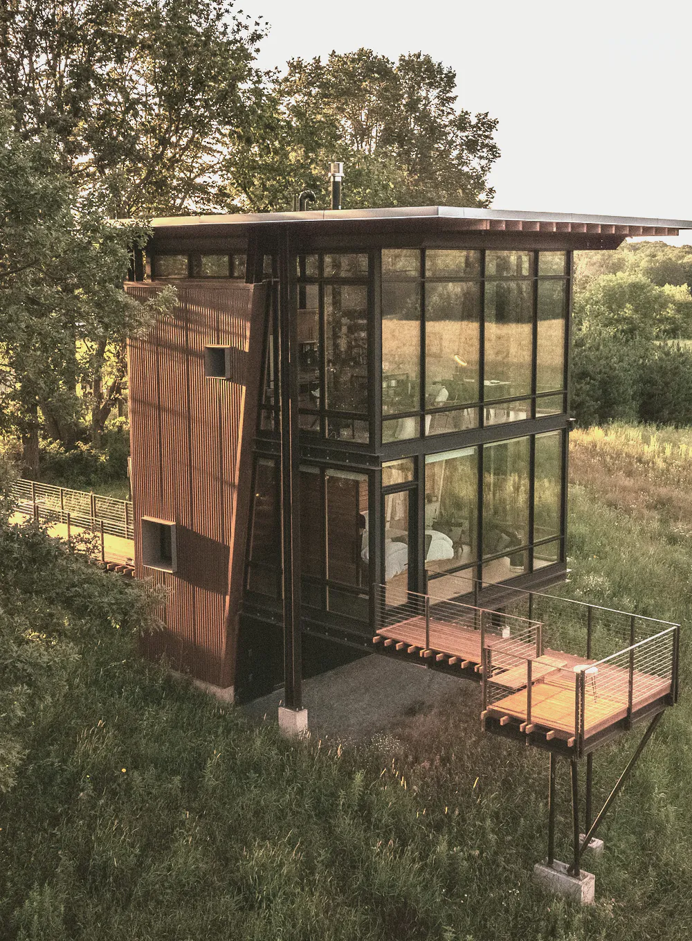A two level timber and glass house with a deck, standing in long grass