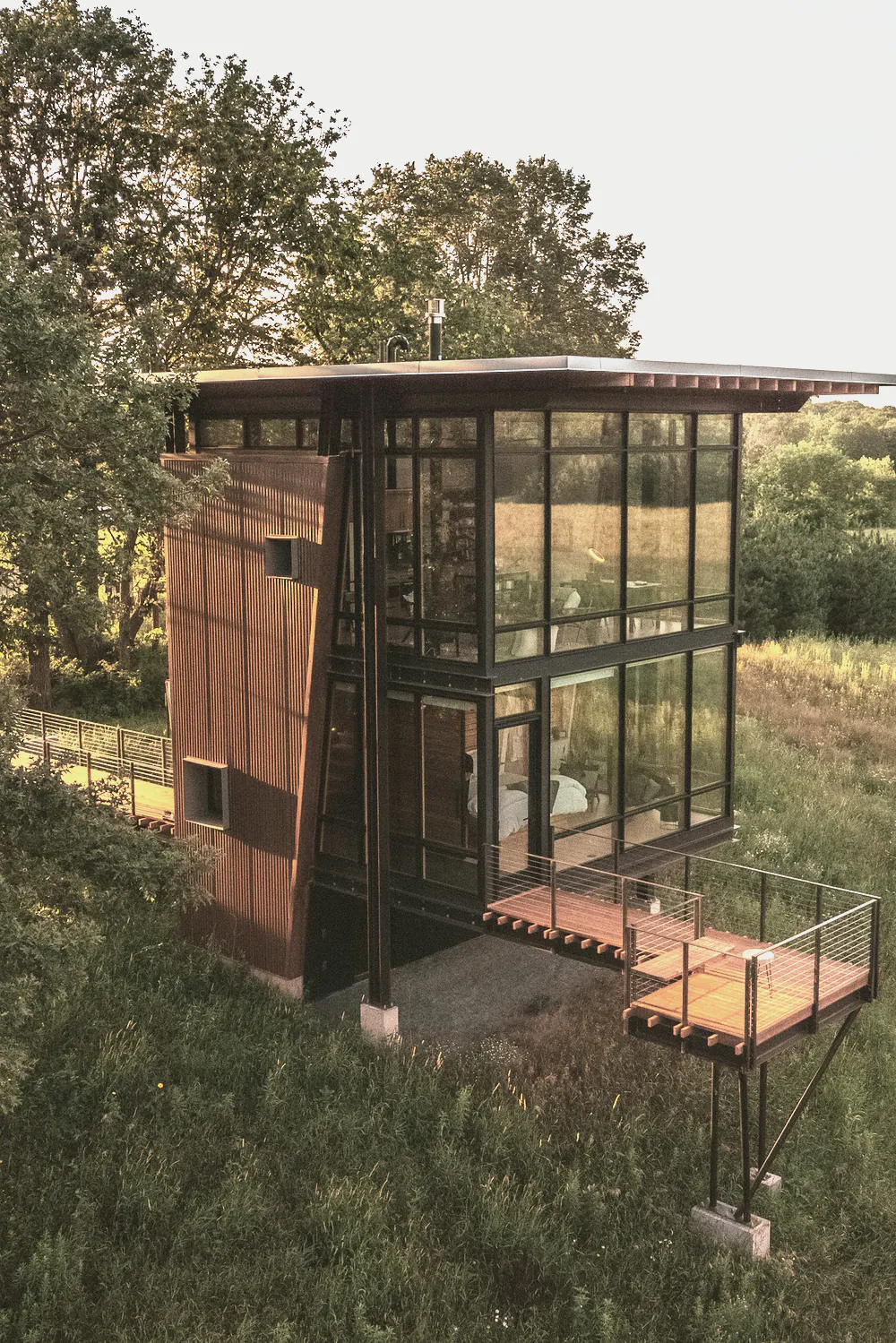 A two level timber and glass house with a deck, standing in long grass
