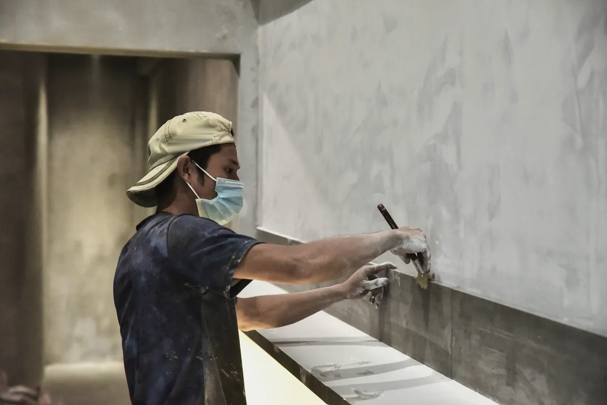 A plasterer in a cap and mask smoothing render along a new wall