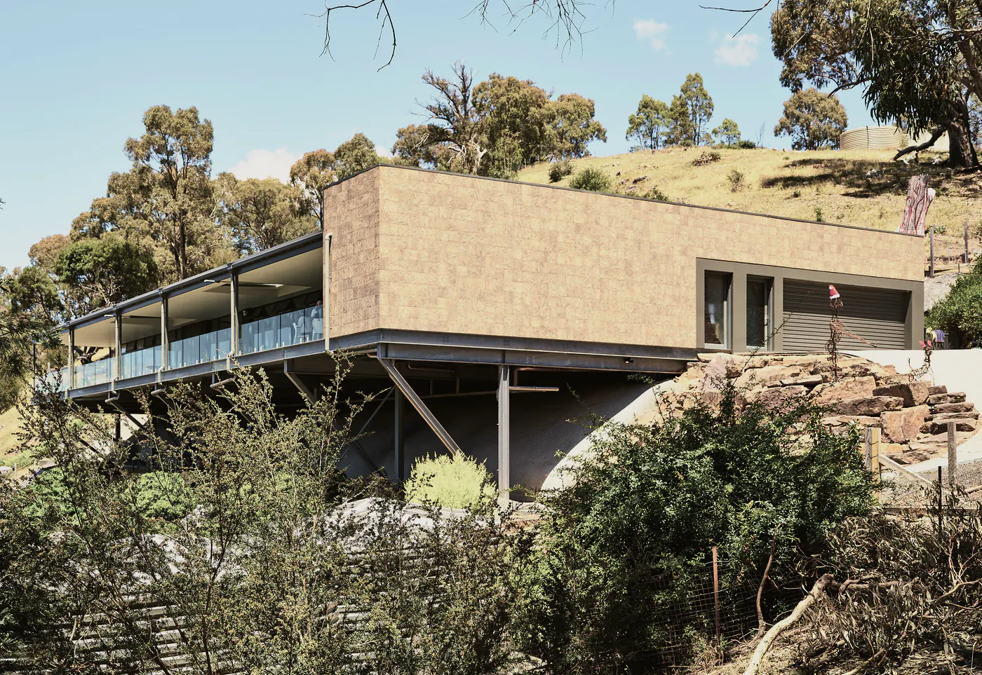 A long, low house on steel legs on a hillside of gum trees, a clad box at one end