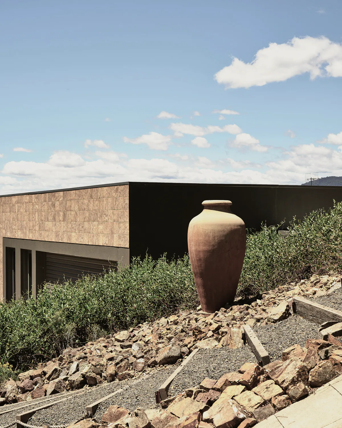 A tall terracotta urn on a planted rock bank beside the house