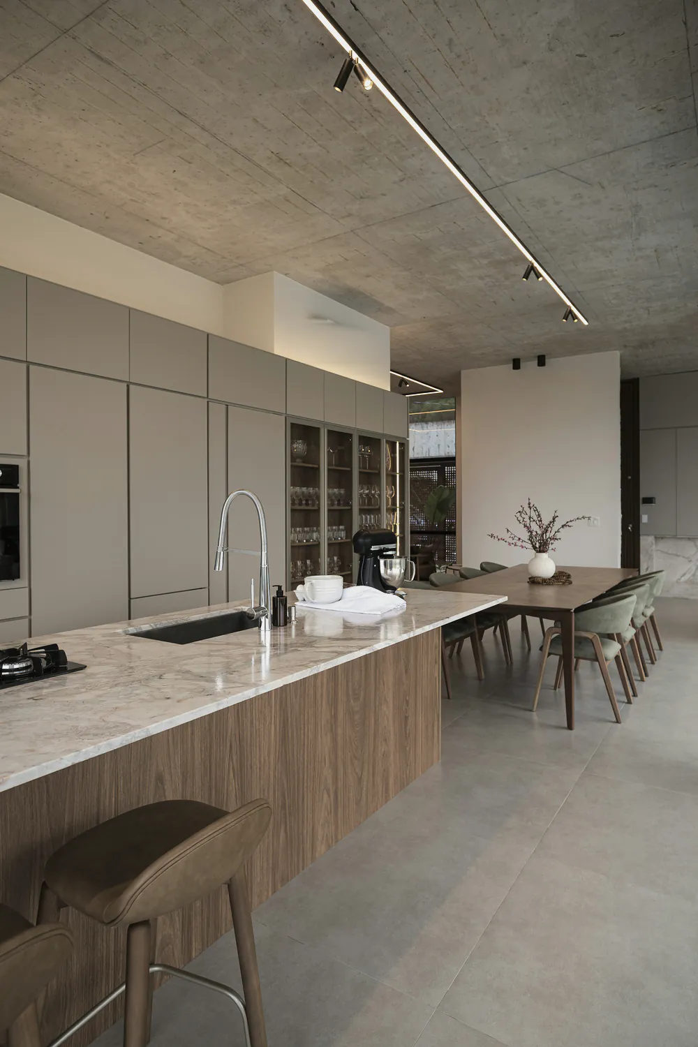A long kitchen island with stools under a concrete ceiling and track lights