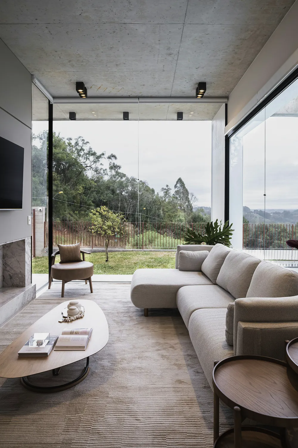 A living room with a long cream sofa and a glass corner looking out to the trees