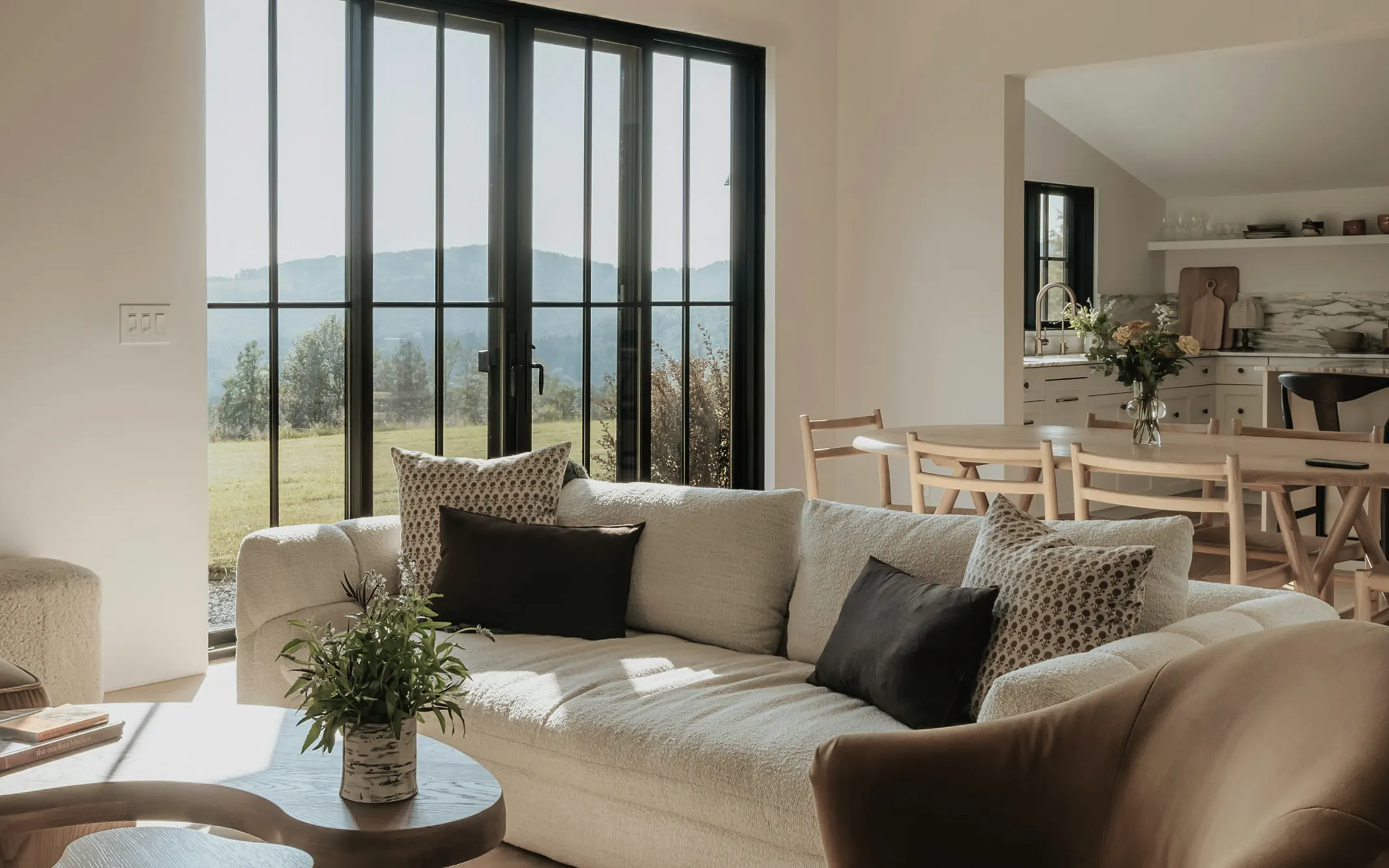 A living room with a cream sofa and a wall of black framed glass doors looking out to green hills
