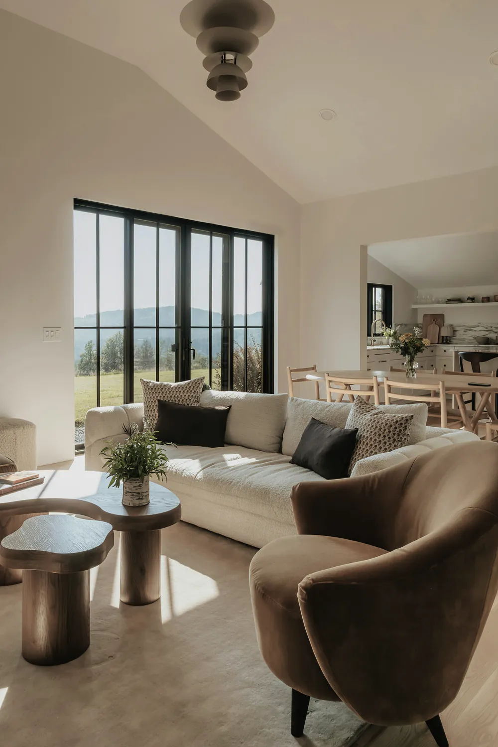 A living room with a cream sofa and a wall of black framed glass doors looking out to green hills