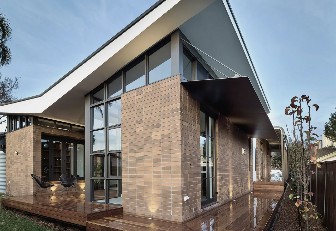 A brick and glass house with a raked white roof above a wide timber deck