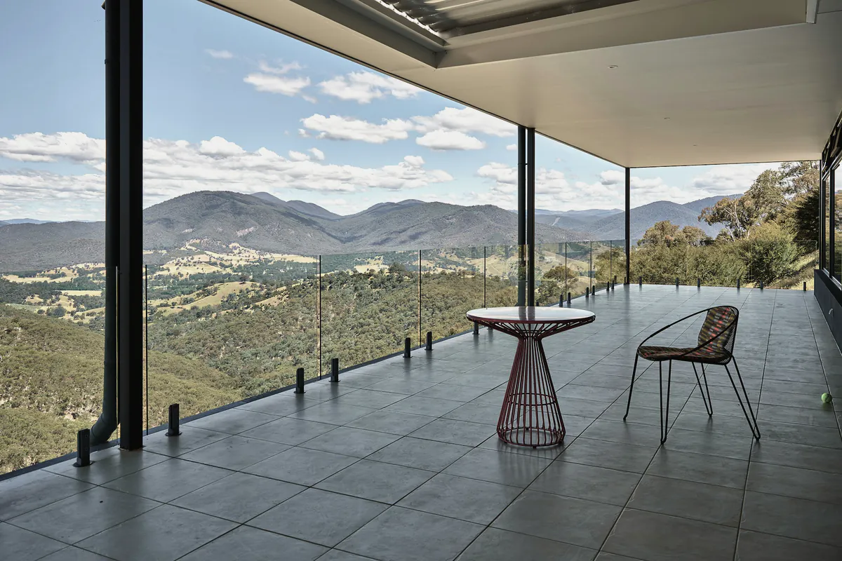 A covered balcony with a small table and chair looking across a valley of gum trees to the ranges